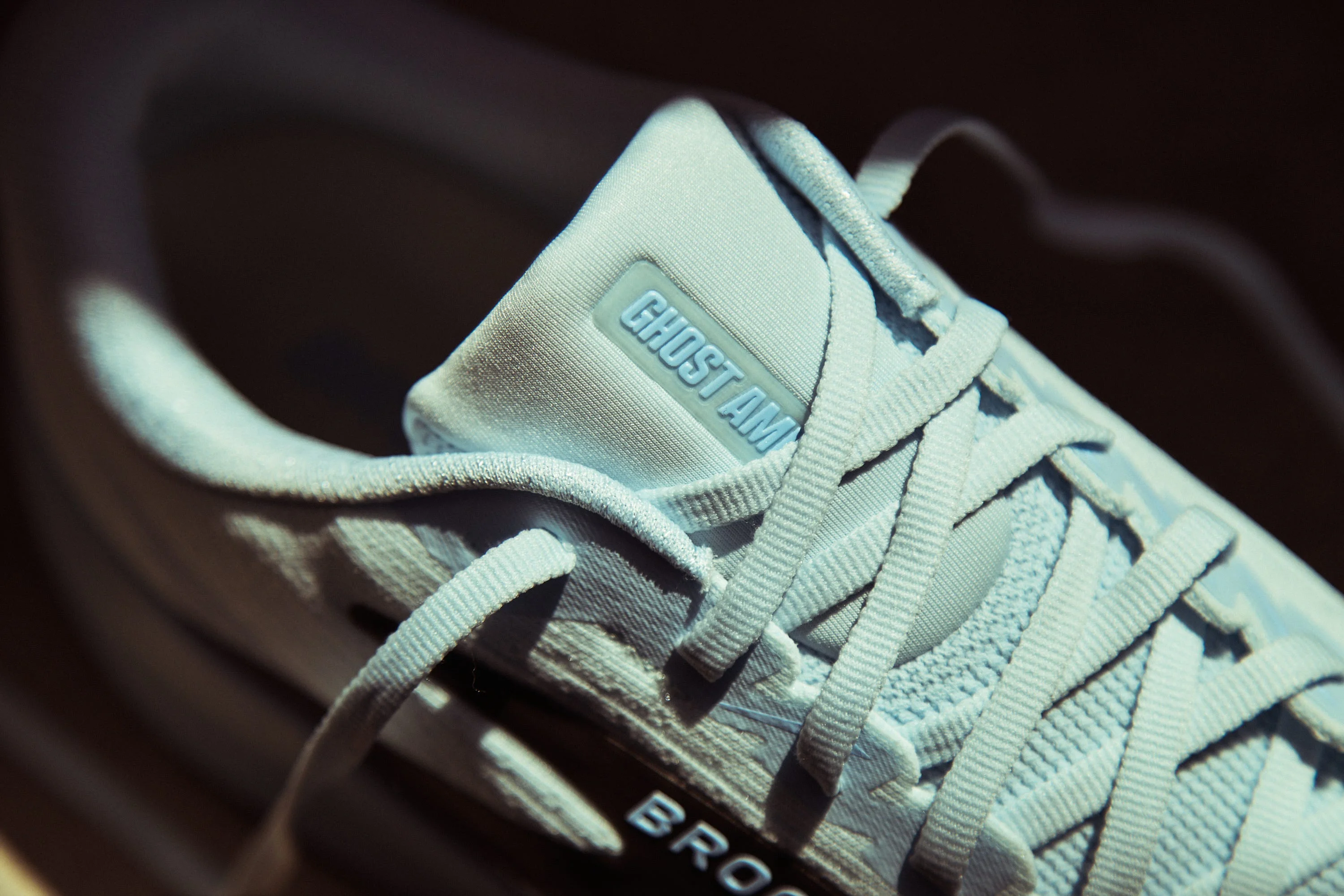Light blue running shoe with "GHOST AM" label on a padded tongue and intricate lacing design.