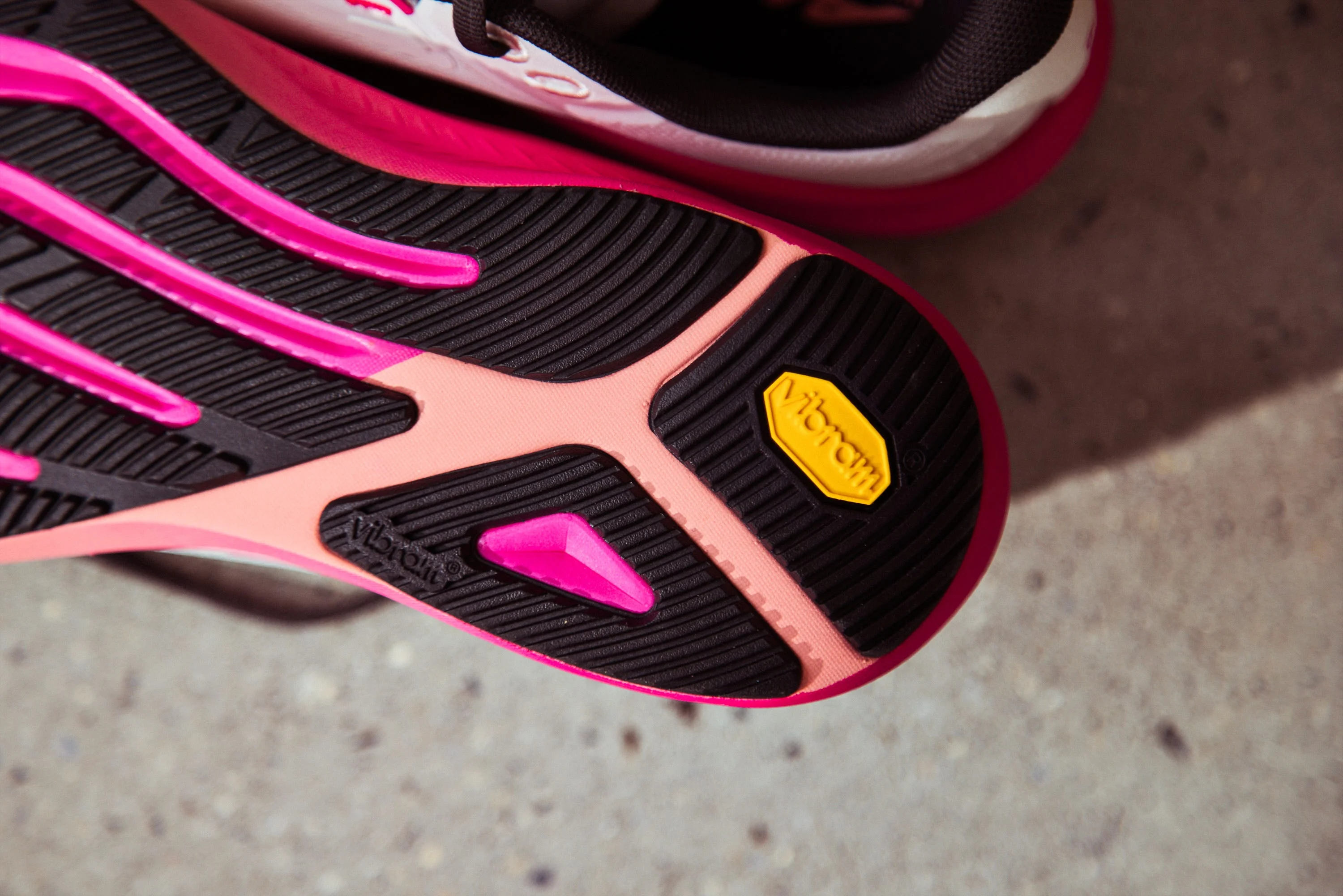 Shoe sole featuring pink and black rubber with a yellow Vibram logo for enhanced traction and durability.