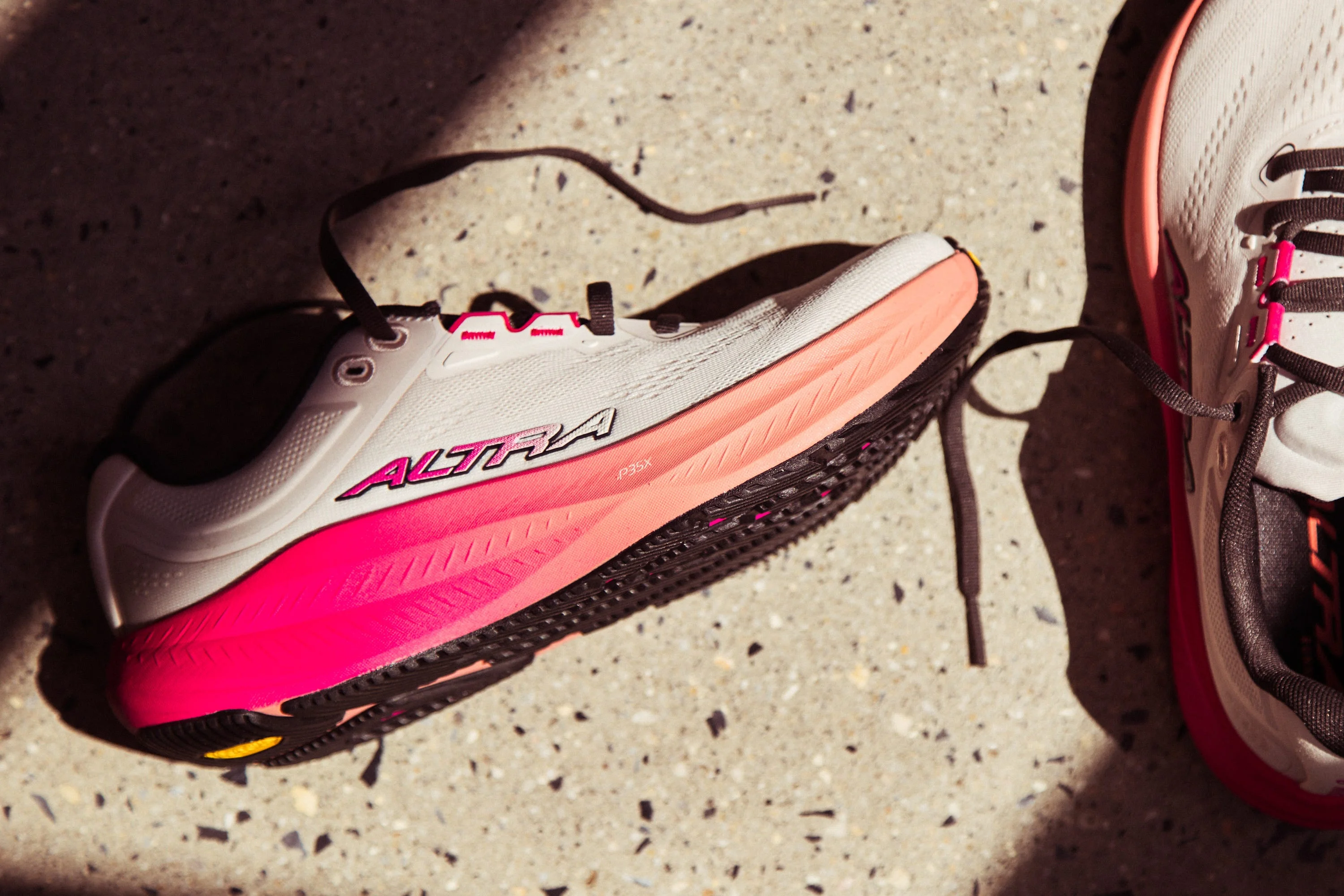 A pair of Altra running shoes featuring a white and pink design on a textured surface.