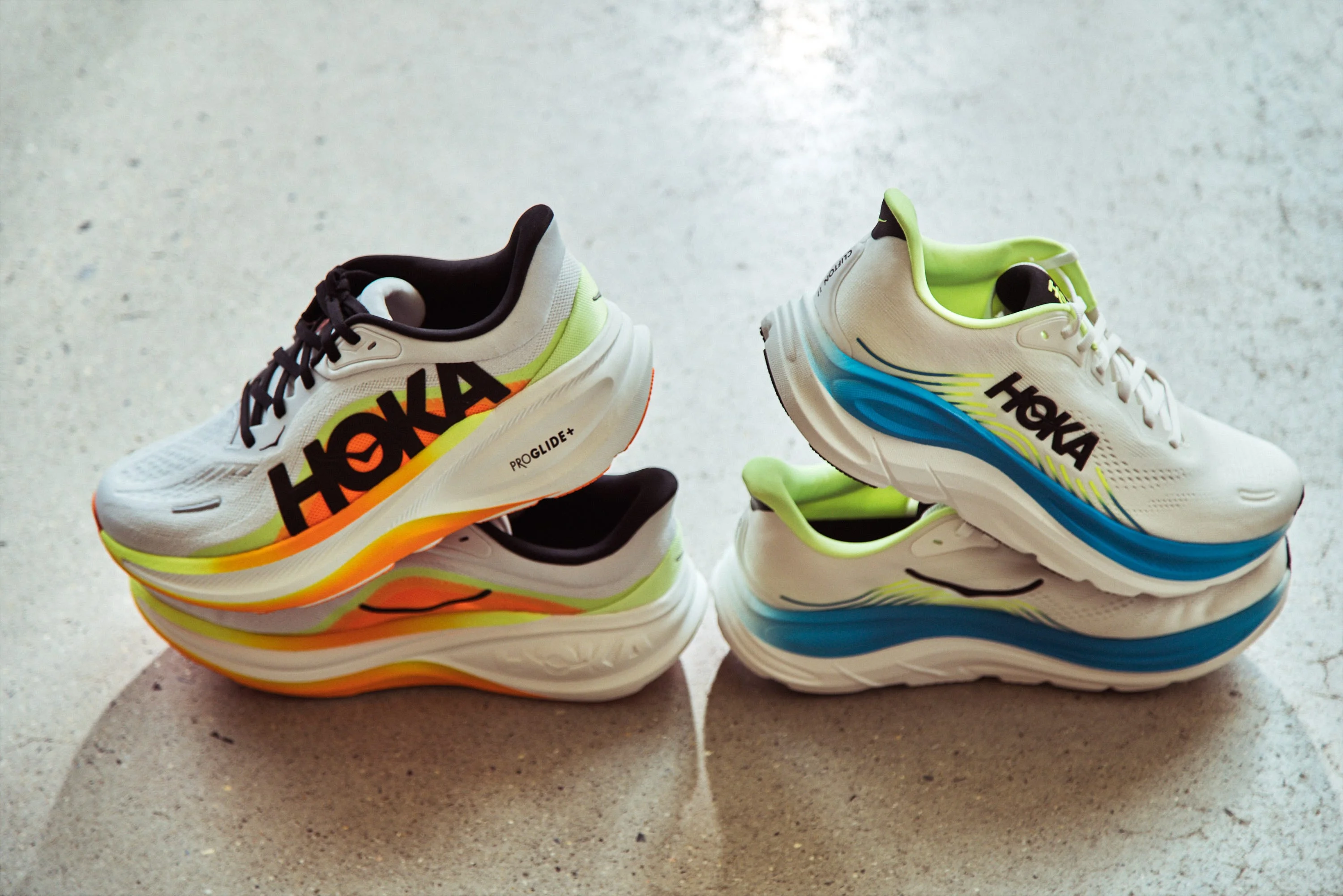 Colorful HOKA running shoes stacked with vibrant accents in orange, yellow, and blue against a neutral background.