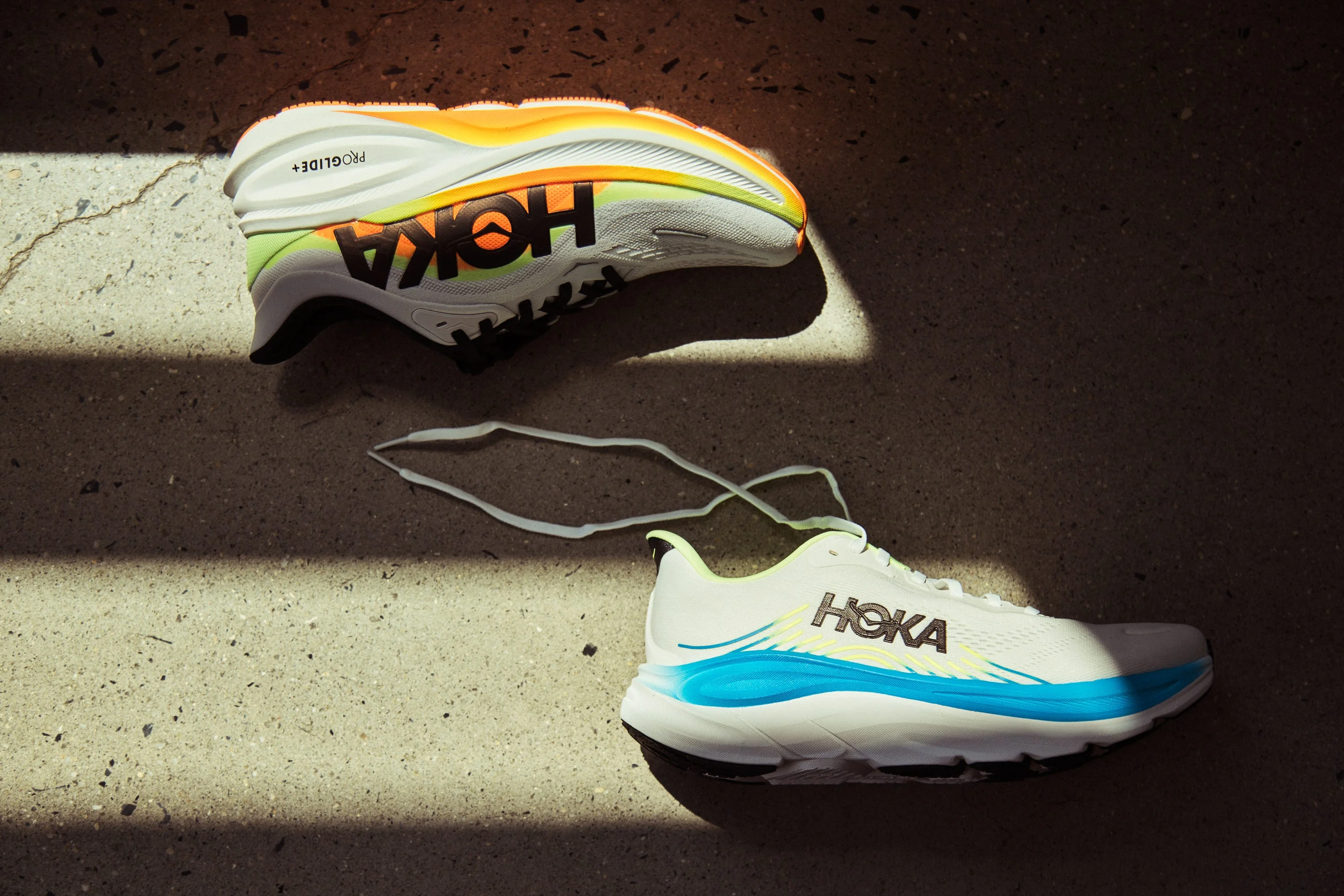 Hoka running shoes in contrasting colors displayed on a concrete surface.