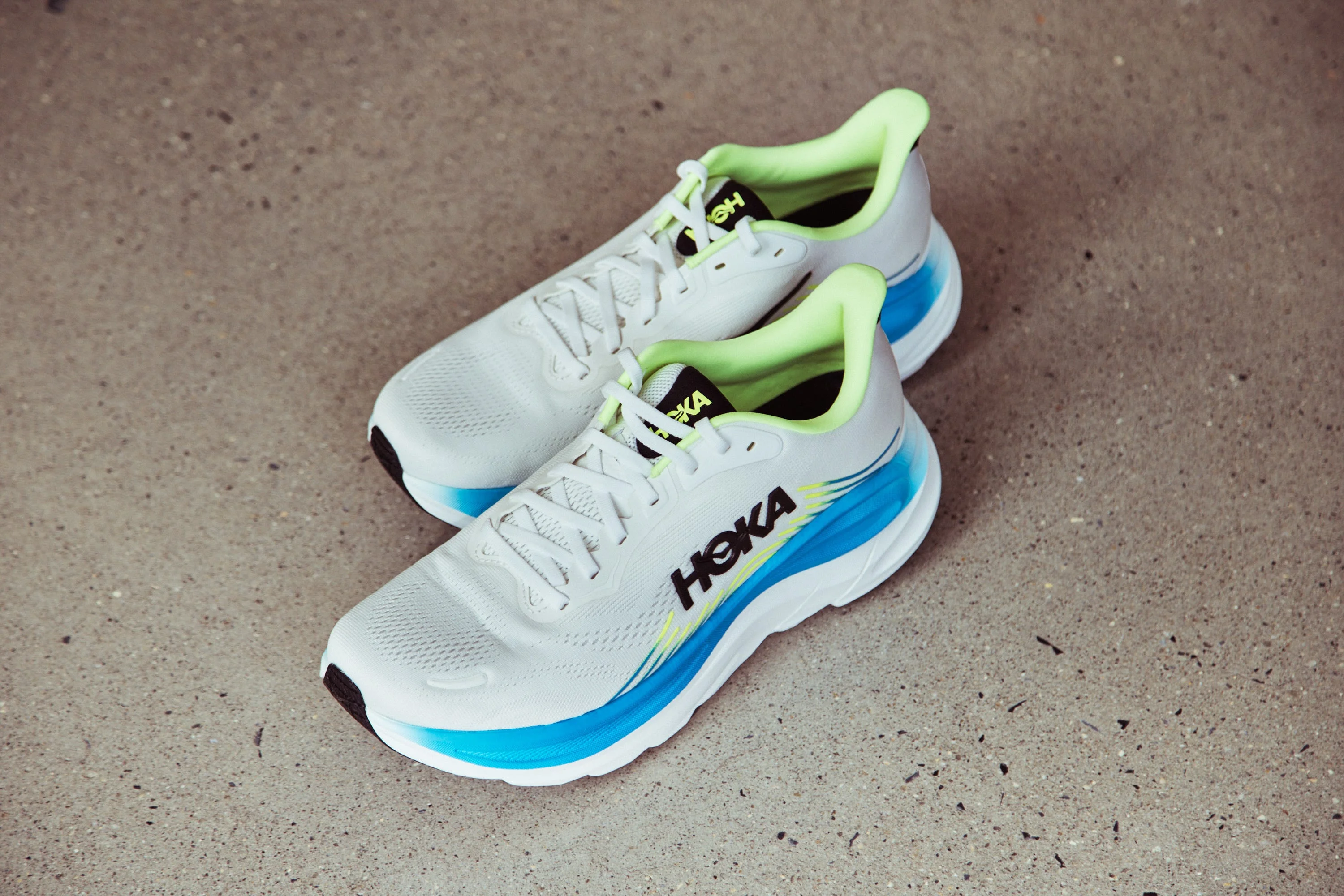 White athletic shoes with blue accents and lime green details on a concrete surface.