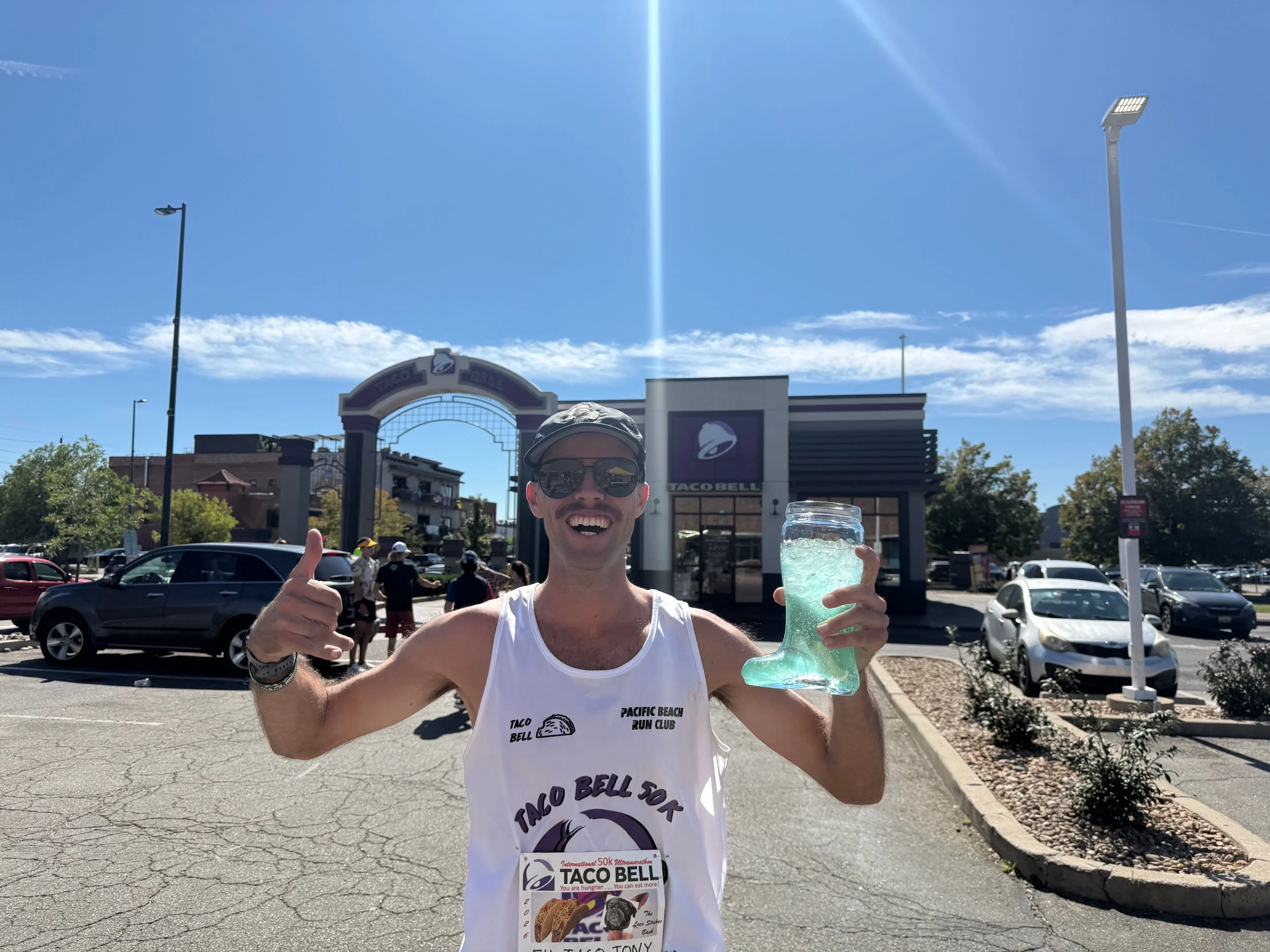 Man giving a thumbs up while holding a large drink in front of a Taco Bell restaurant on a sunny day. Man giving a thumbs up while holding a large drink in front of a Taco Bell restaurant on a sunny day.