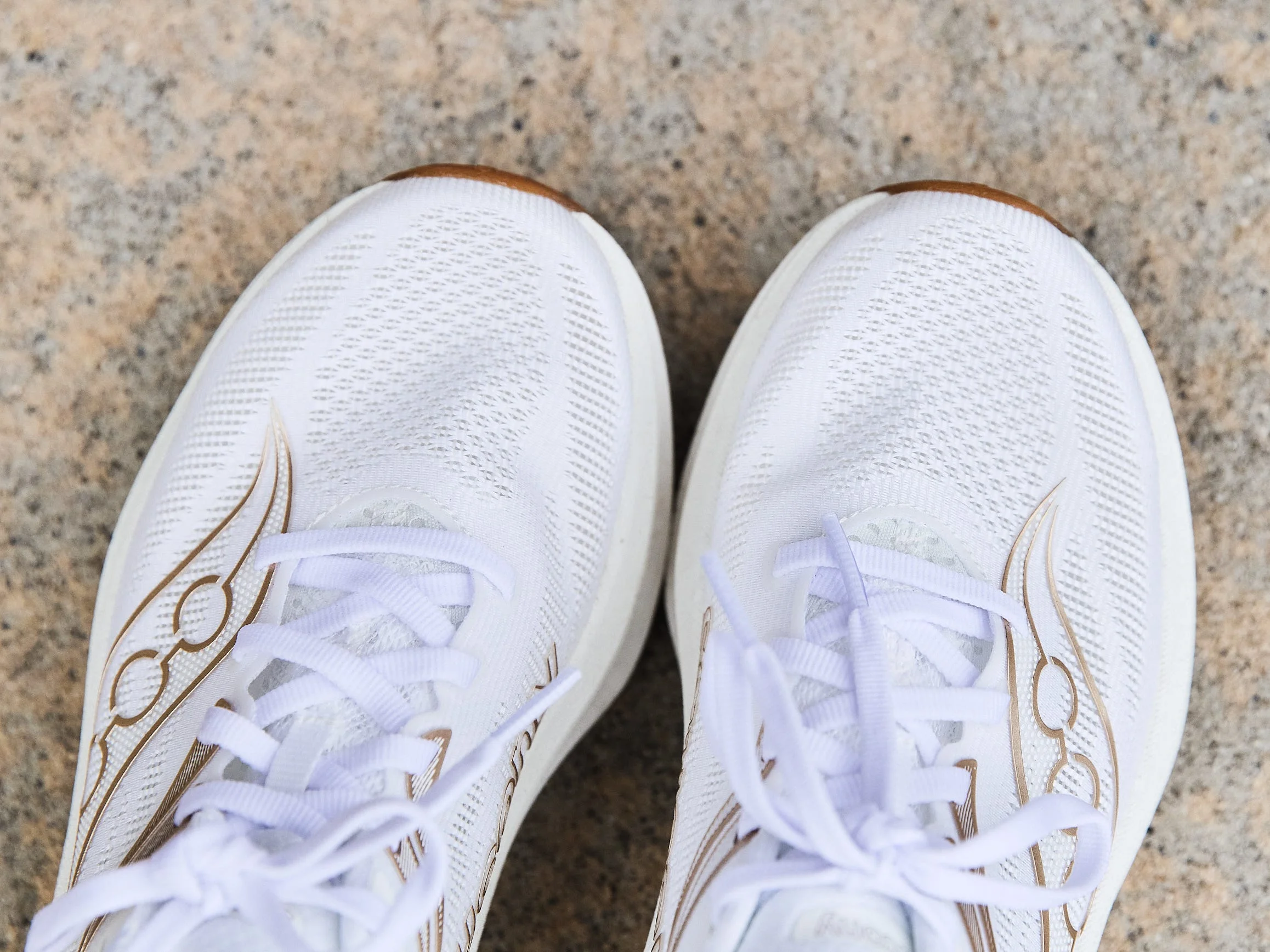 White athletic shoes with light laces and decorative details on a textured surface.