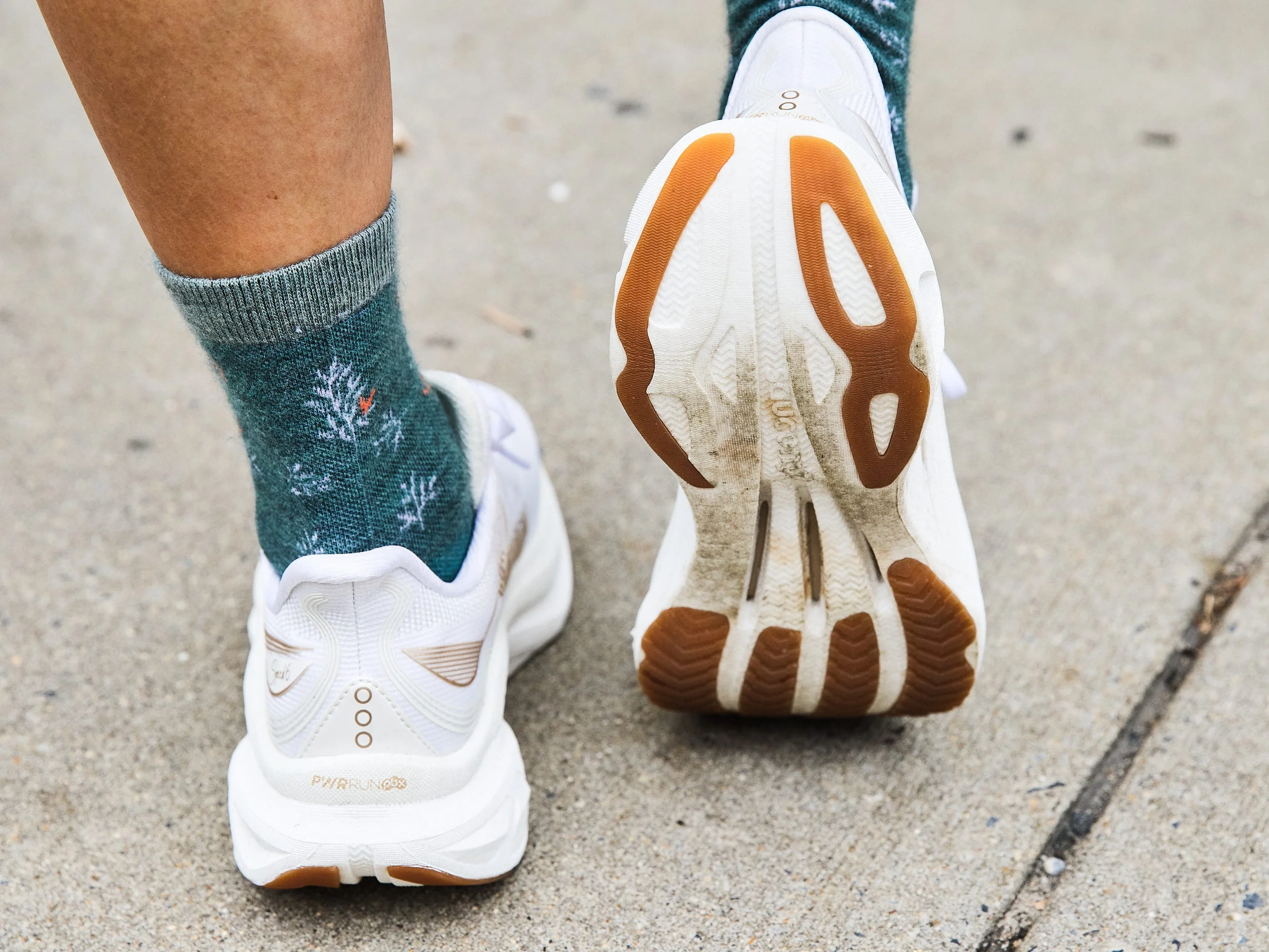 Close-up of a foot in white sneakers and patterned green socks on a concrete surface.