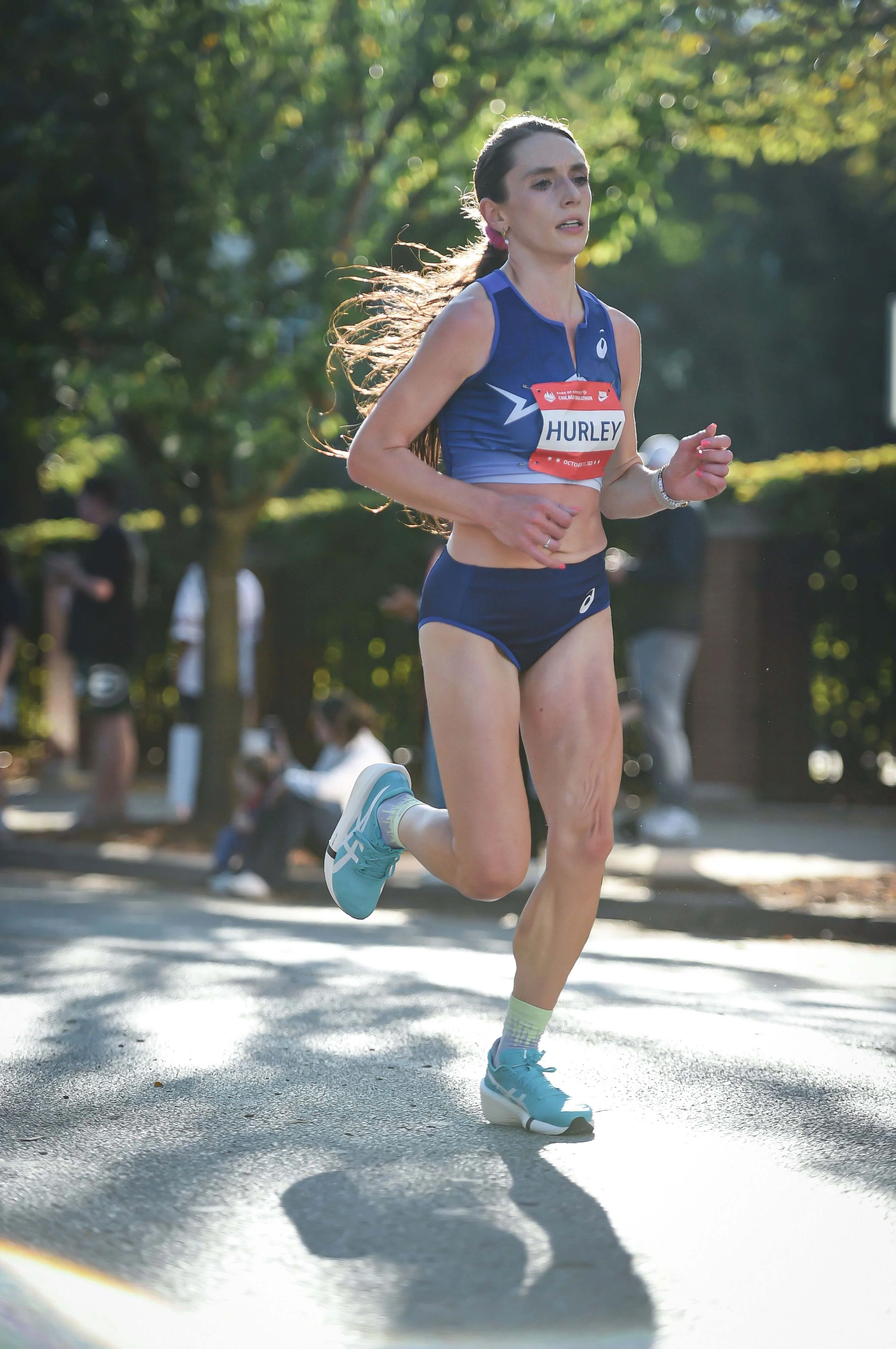 A runner in a blue athletic outfit competing in a road race, with spectators in the background.