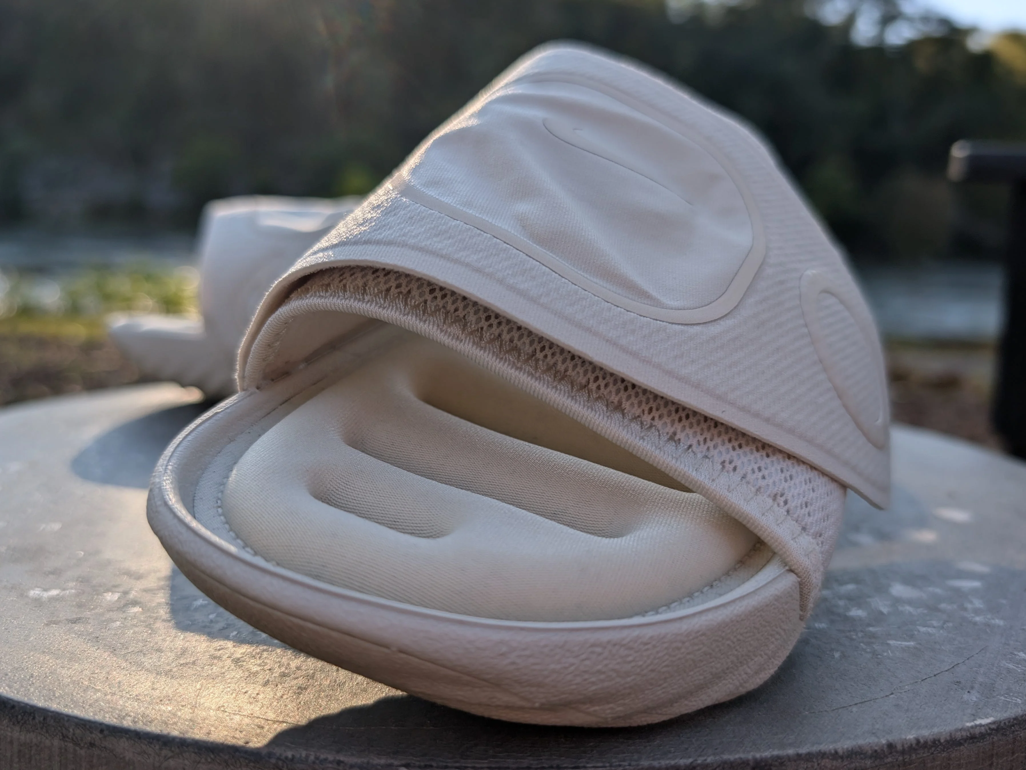 Light-colored sandals resting on a round wooden surface with a blurred natural background. Light-colored sandals resting on a round wooden surface with a blurred natural background.