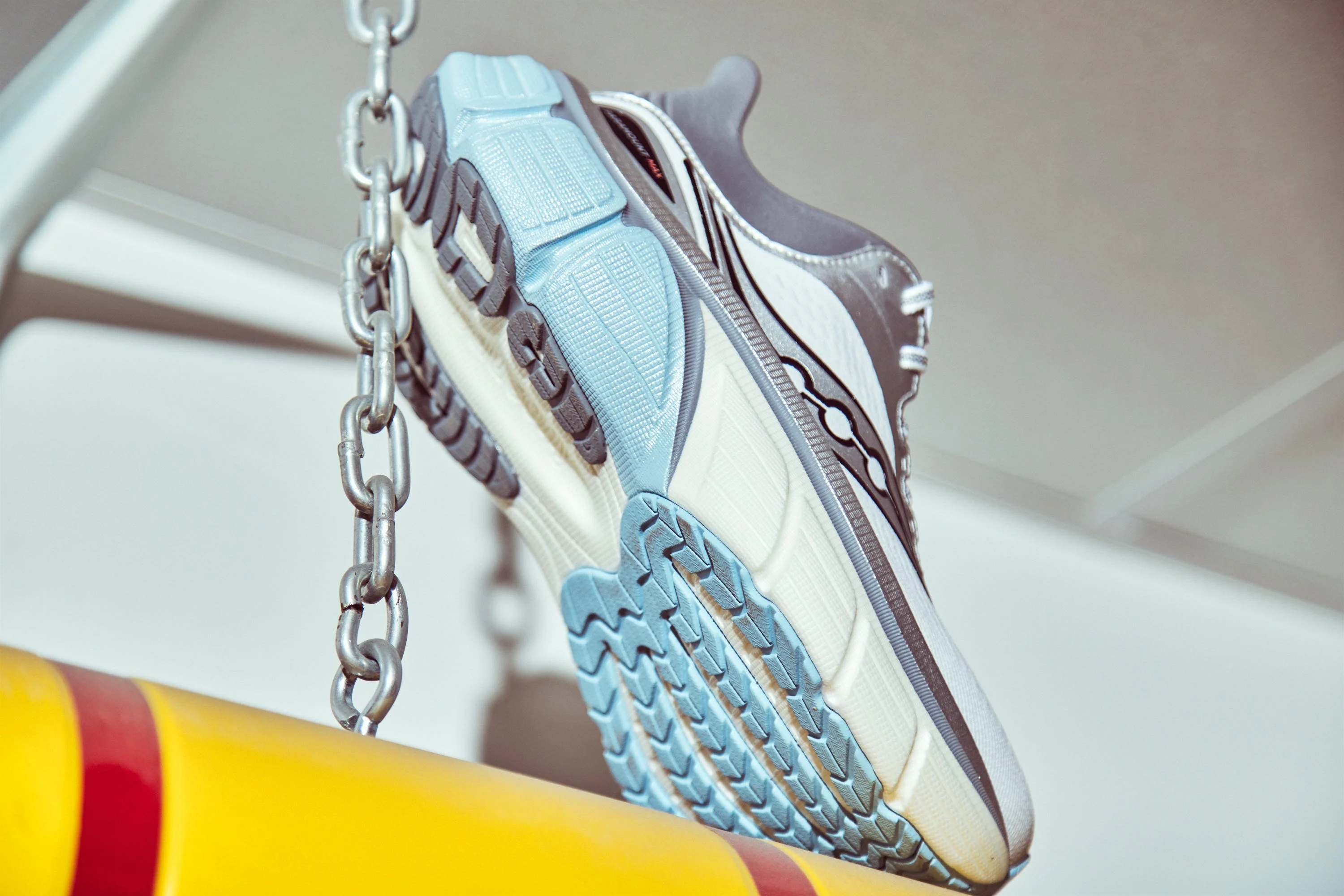 A modern running shoe hanging from a chain against a blurred background.