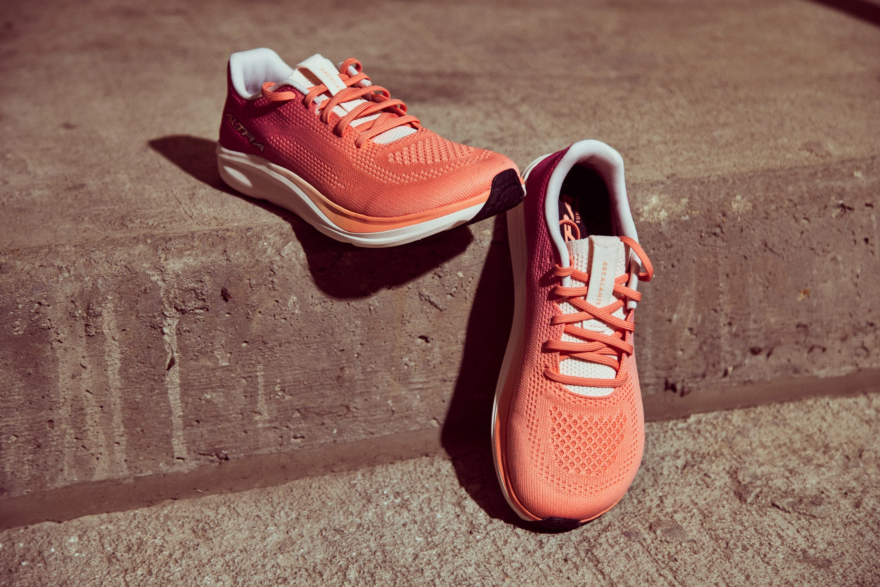 Coral athletic shoes with vibrant mesh upper and white sole, positioned on a concrete surface.
