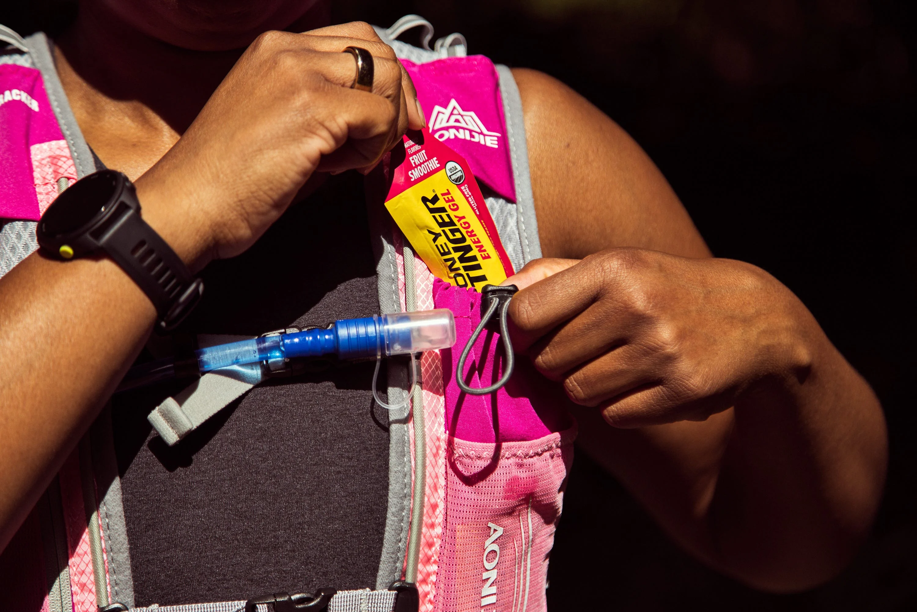 A person inserting an energy gel packet into a hydration vest during outdoor activity